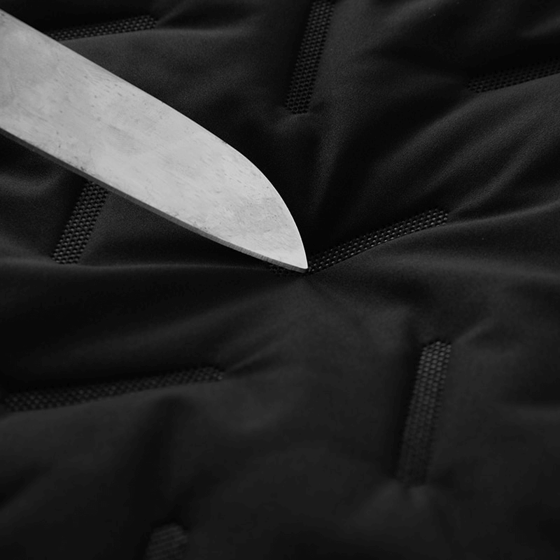 Close-up of knife blade testing black fabric durability with quilted pattern, showcasing toughness of material in low light setting.